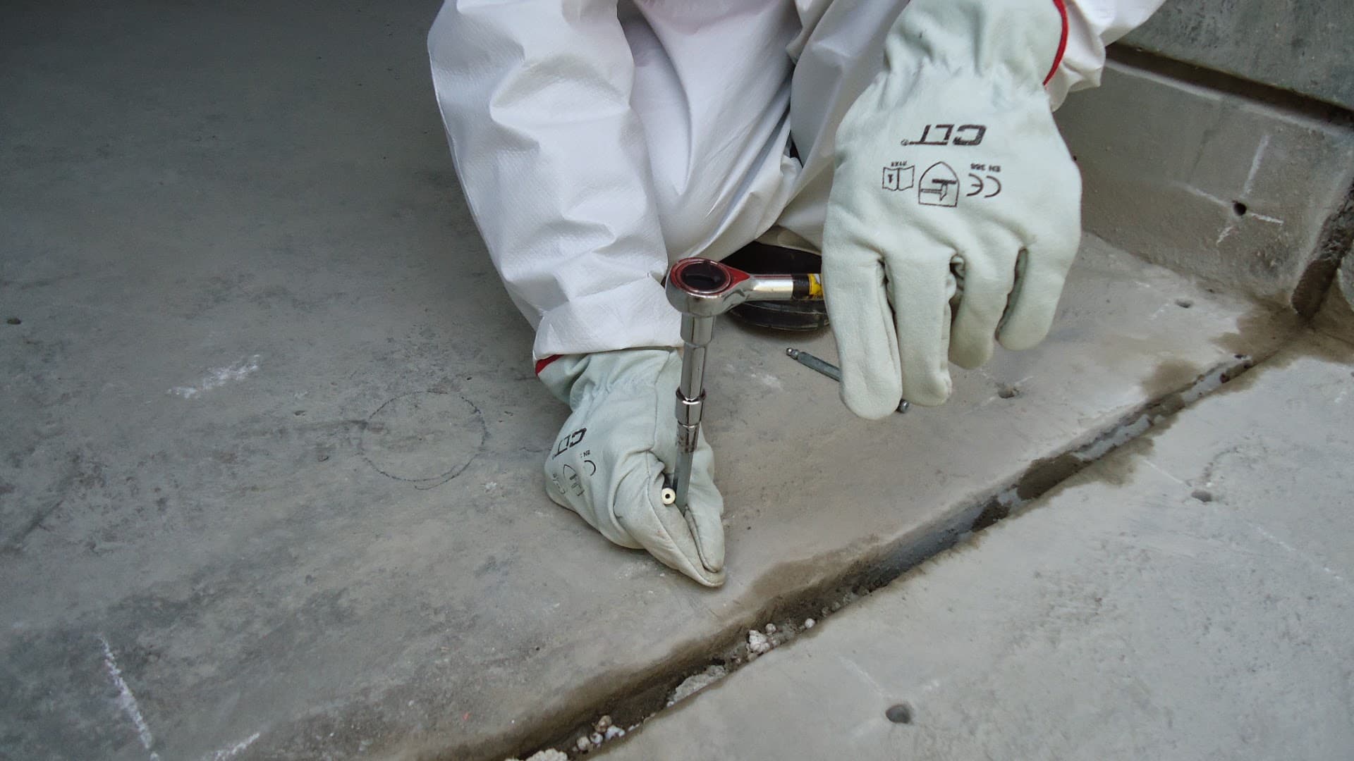 Manos con guantes ajustando un inyector sobre una junta de concreto